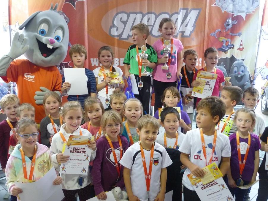 Kinder mit Medaillen, Pokalen und Urkunden neben dem speed4-Maskottchen in Memmingen